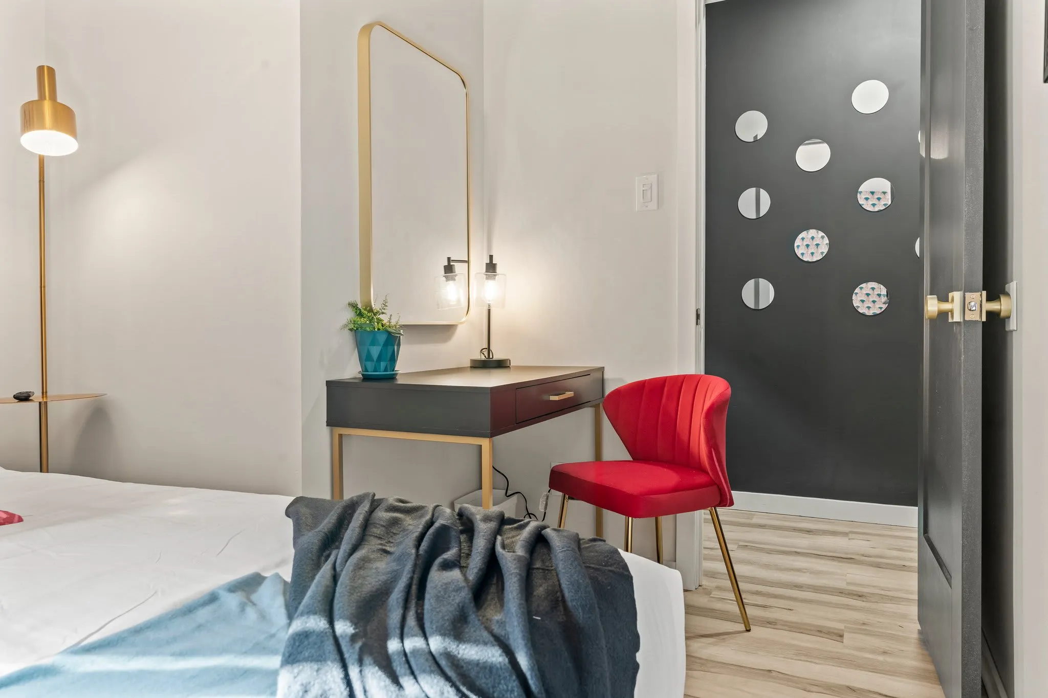 This elegant corner features a chic desk and a glamorous light fixture. The stylish red chair and tall plant add a pop of color, making it an inviting space to prepare for your day or catch up on work in a cozy atmosphere.