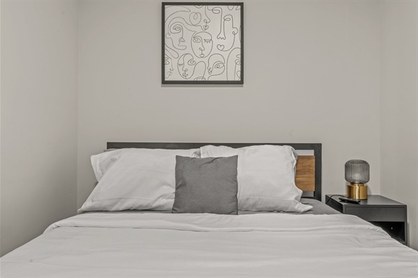 Modern simplicity meets comfort with fresh linens, accent art, and a minimalist bedside setup.