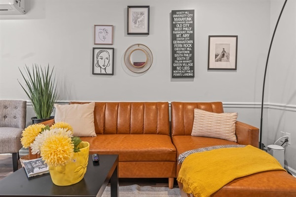 Appreciate the stylish decor of this inviting living room. The plush leather sofa, vibrant yellow accents, and thoughtfully curated wall art create a cozy atmosphere you will adore.