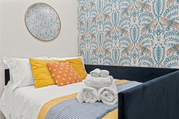 You will appreciate the cozy bed with its colorful cushions and fresh linens. The stylish wallpaper and thoughtful decor, including the round mirror and neatly arranged towels, create a welcom
