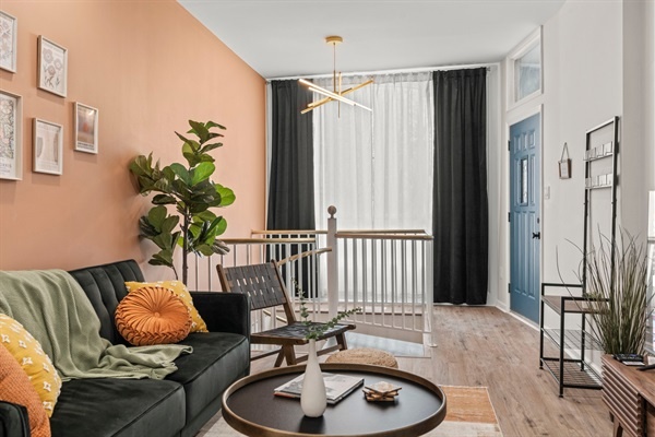 Welcome to a bright, stylish living area with comfortable seating, colorful cushions, and unique decor. Enjoy modern art, a lush plant, and a warm, inviting ambiance, highlighted by a stunning