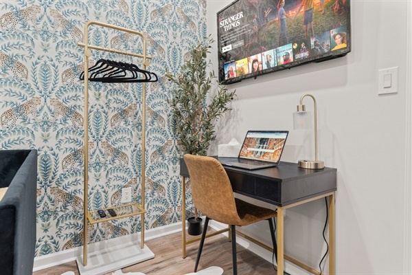 You will love this bright and stylish workspace, featuring a sleek desk with gold accents, a comfortable chair, and a TV for entertainment. The chic wallpaper and thoughtful decor create an in