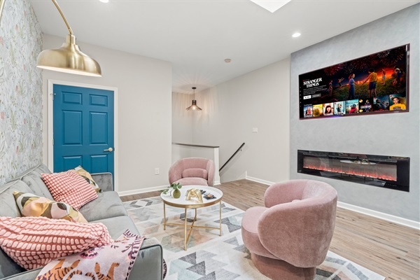 You will appreciate the cozy seating area with a vibrant blue door and modern fireplace. The pastel pink chairs and plush sofa offer a perfect spot to unwind after a long day of exploring the city.