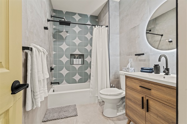 A spa-inspired retreat featuring bold tile design, rainfall shower, and backlit mirror — sleek comfort meets thoughtful style.