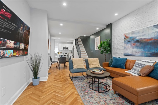 You will appreciate the open-concept living area with a stylish herringbone floor, modern decor, and a large TV. The inviting atmosphere is perfect for relaxation and entertainment.