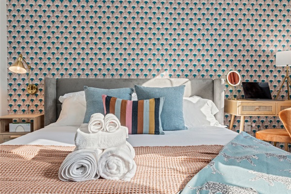 You will love the serene and stylish bedroom, adorned with patterned wallpaper and colorful pillows. Fresh towels and linens await you, ensuring a comfortable and relaxing night's sleep in this beautiful setting.