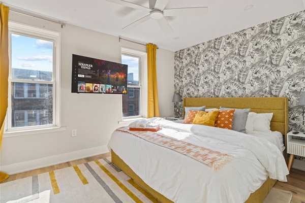King bedroom with bold accent wall, mustard tones, and sunlight—your bright retreat in South Philly.